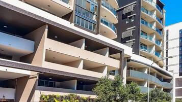 A multi-story residential building with balconies, a covered parking area, and a small outdoor seating area with plants.