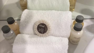 Un baño con una toalla blanca, un albornoz y varias botellas de Jabón Corporal Ritual Australian dispuestas sobre una superficie de vidrio.