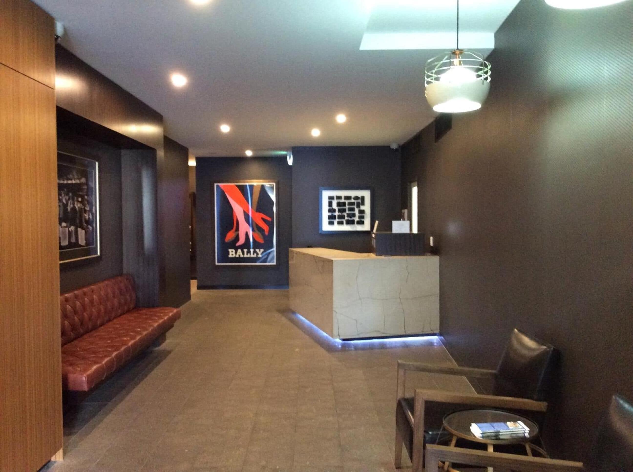 A reception area with a dark wall, a logo, a reception desk, a red leather bench, and a small table with chairs.
