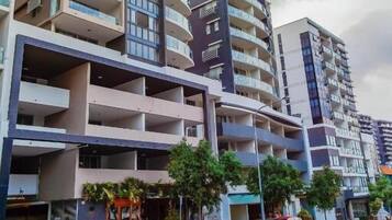 A multi-story residential building with balconies, a parking area, and a street view.