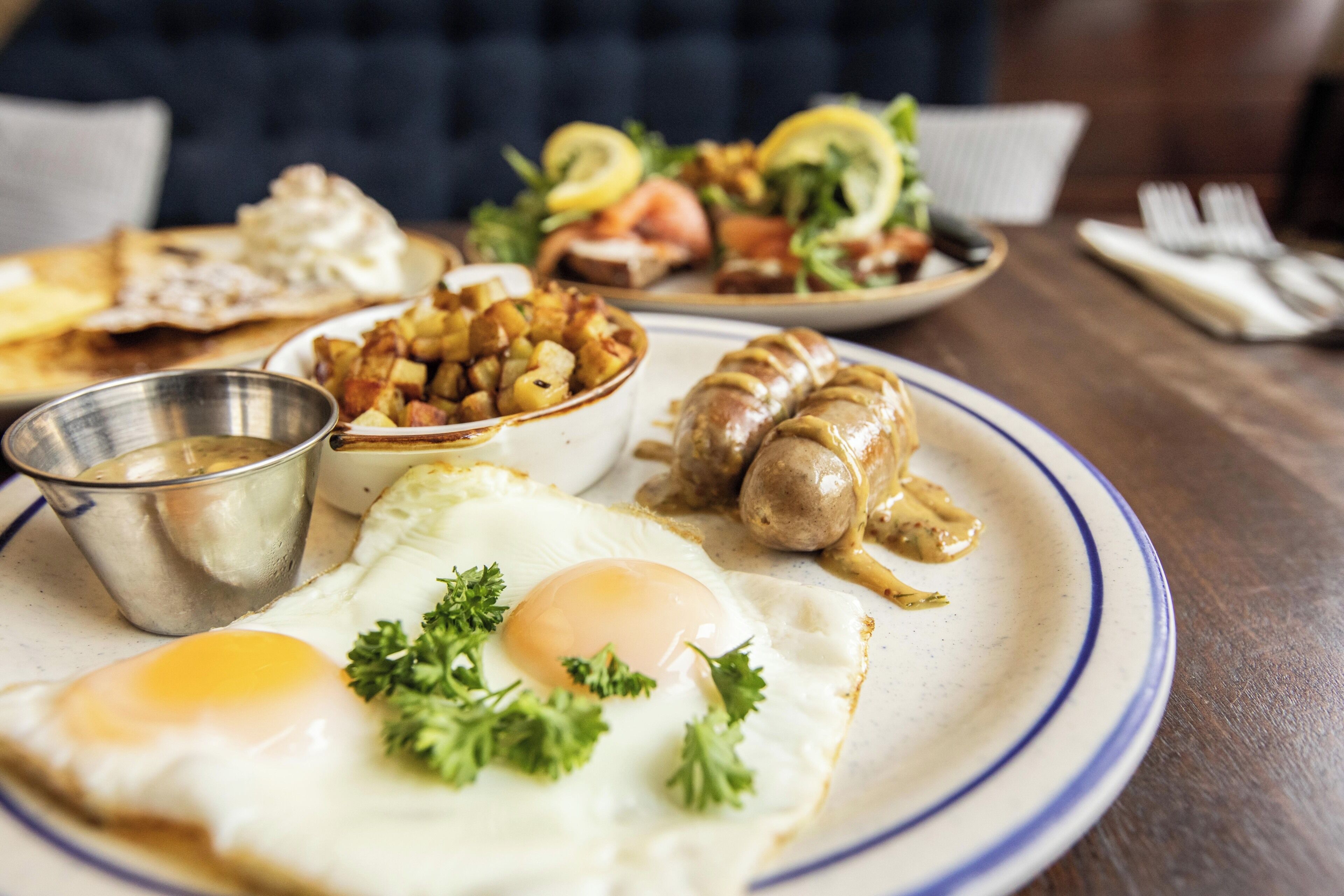 Une assiette de petit-déjeuner comprenant des œufs, des saucisses, des pommes de terre et un petit bol de sauce.