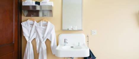 Un baño con lavamanos, espejo y dos toallas blancas colgadas en un perchero.
