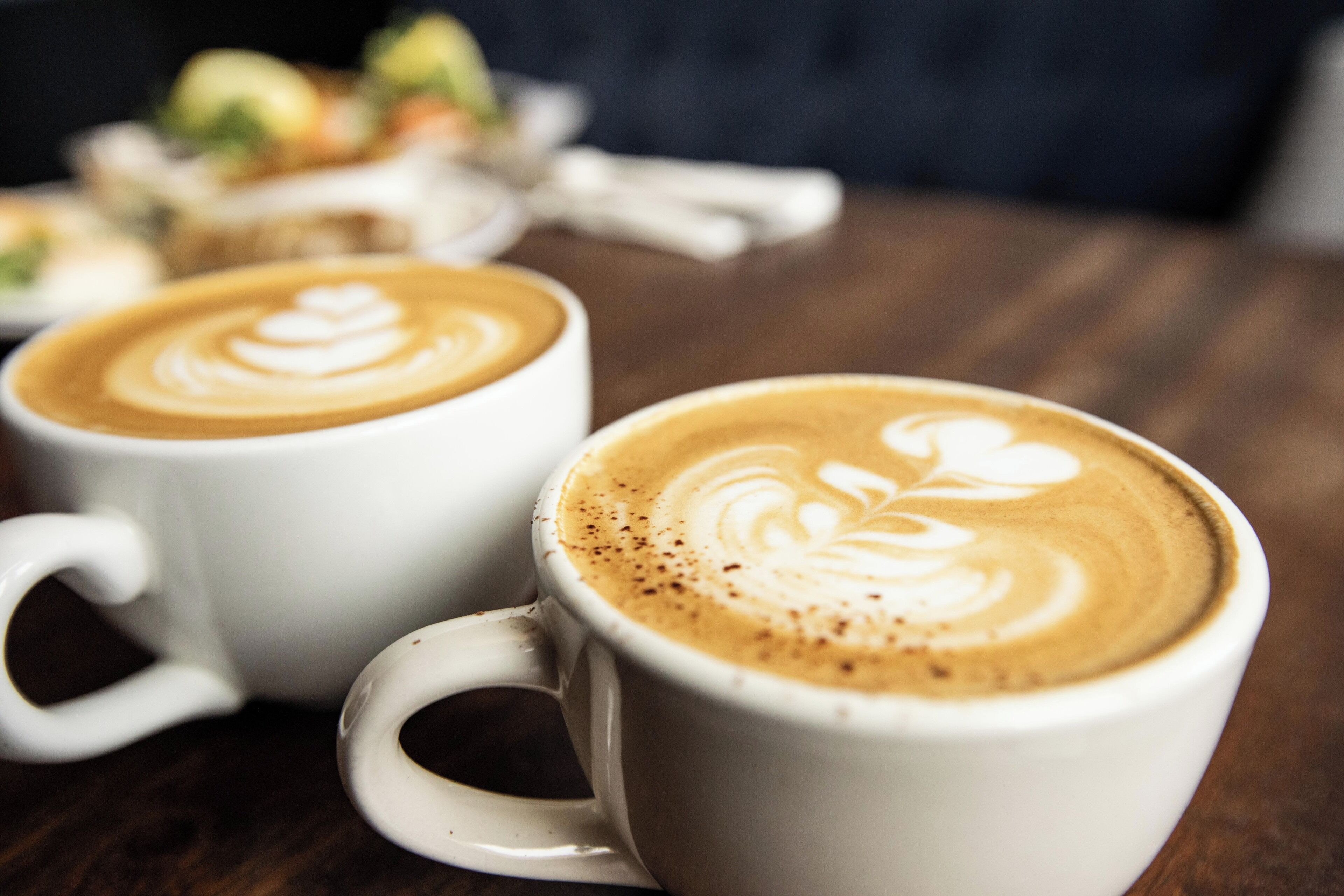 Two white ceramic cups with latte art on a wooden table.