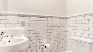 A bathroom with white tiled walls, a white sink, and a toilet.