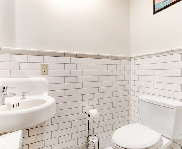 A bathroom with white tiled walls, a white sink, and a toilet. - Commodore Hotel (Astoria)