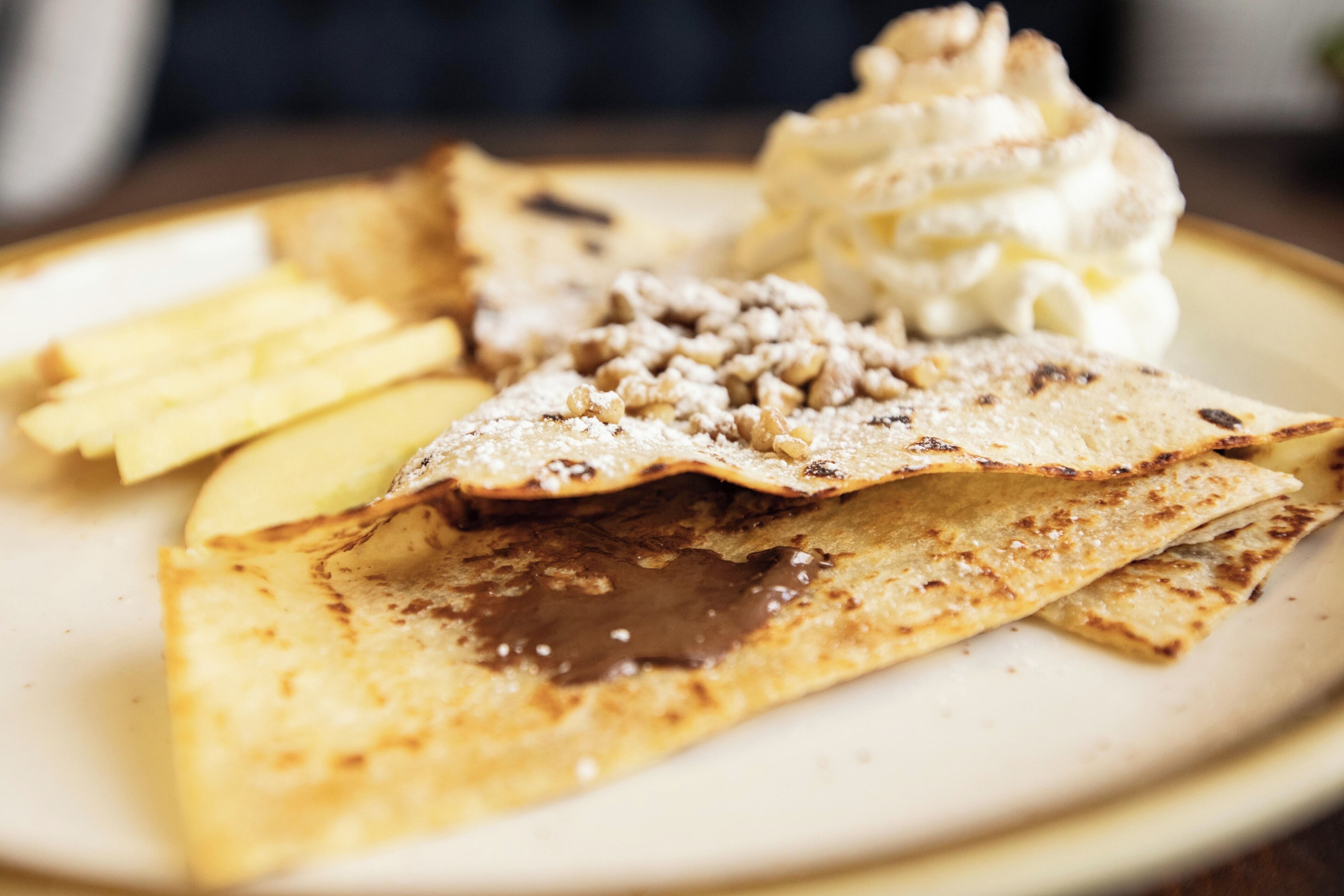 Un plato con crepes, crema batida y salsa de chocolate.