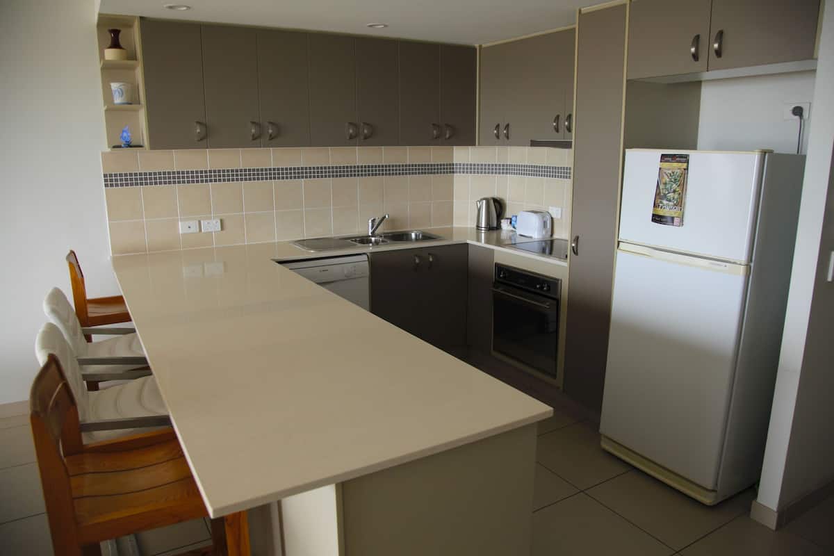 A kitchen with a long counter, a refrigerator, a stove, and a sink.