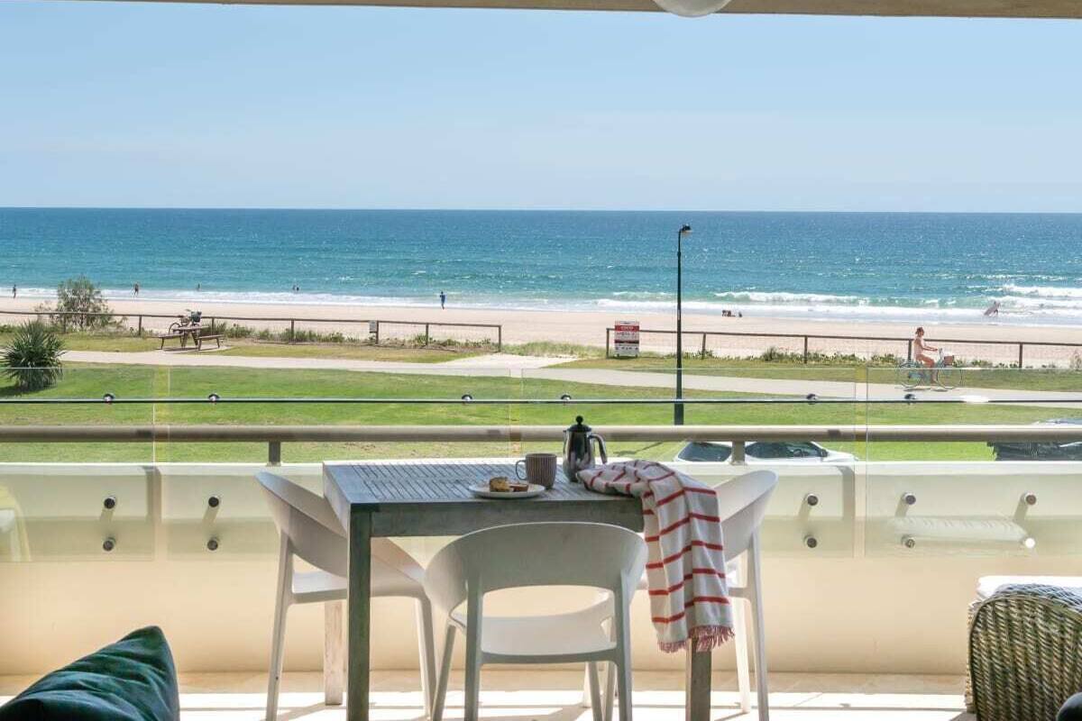 A balcony with a table and chairs overlooking a beach.