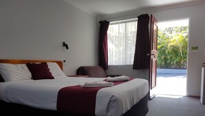 Hotellihuone, jossa on suuri sänky, puinen pääty, työpöytä ja näkymä vehreään maisemaan.