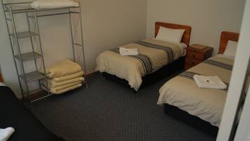 A hotel room with two single beds, a bunk bed, and a small wooden nightstand.