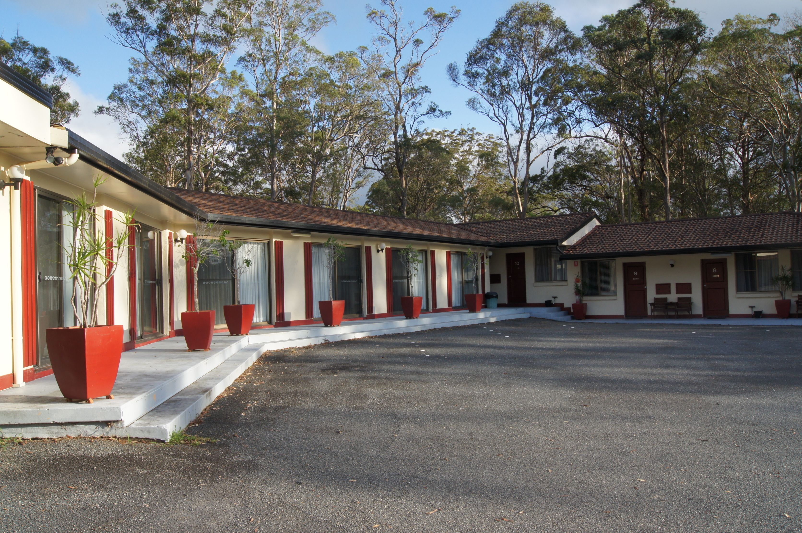 A row of motel rooms with a central driveway and trees in the background.