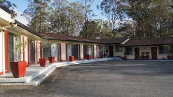 A row of motel rooms with a central driveway and trees in the background.