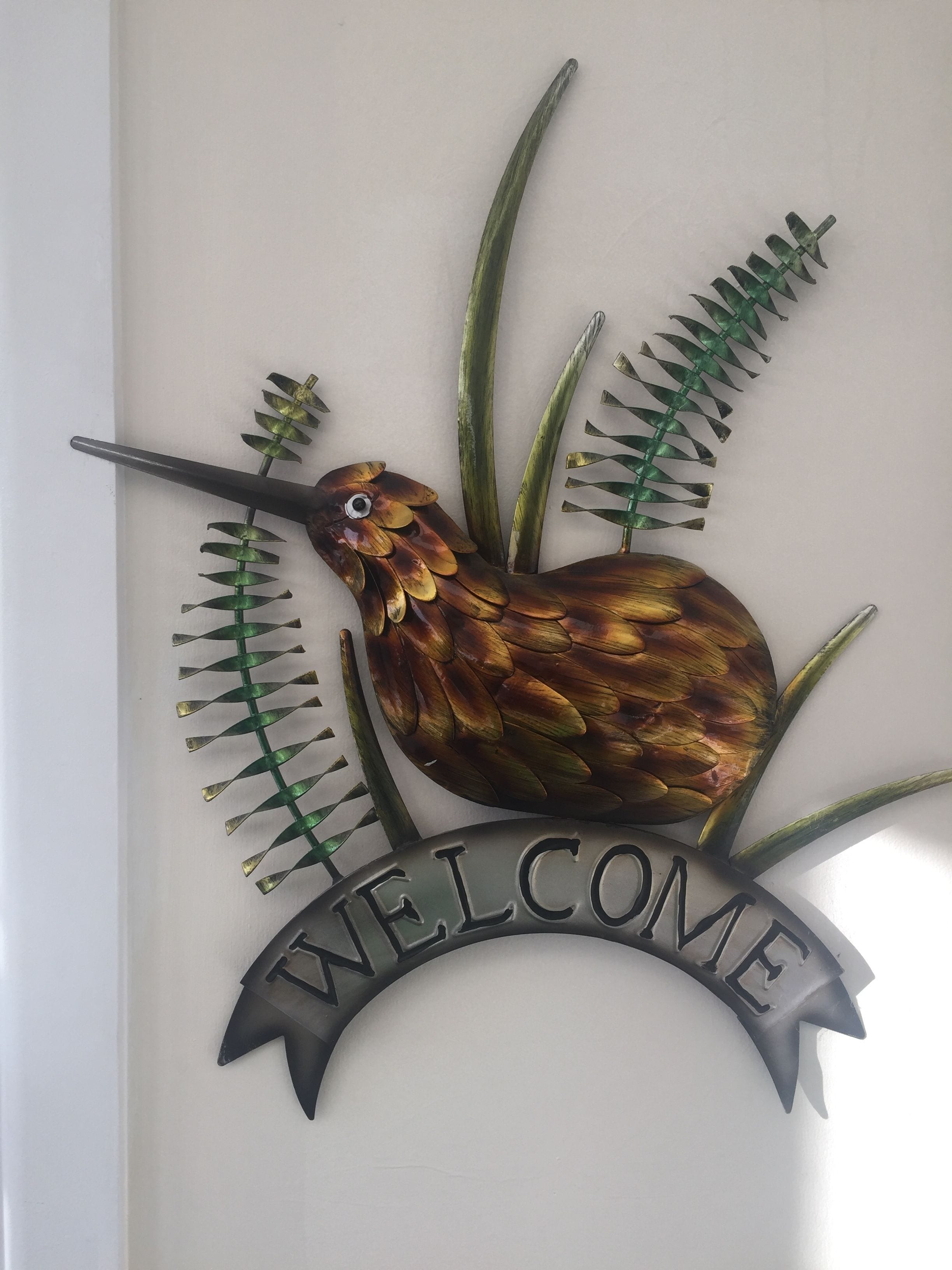 A metal sign with a bird and fern design, featuring the words "WELCOME".