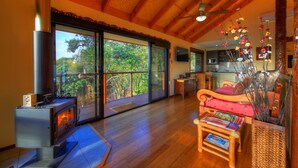 Uma sala de estar acolhedora com lareira a lenha, um sofá e um espaço de jantar com vista para o verde.