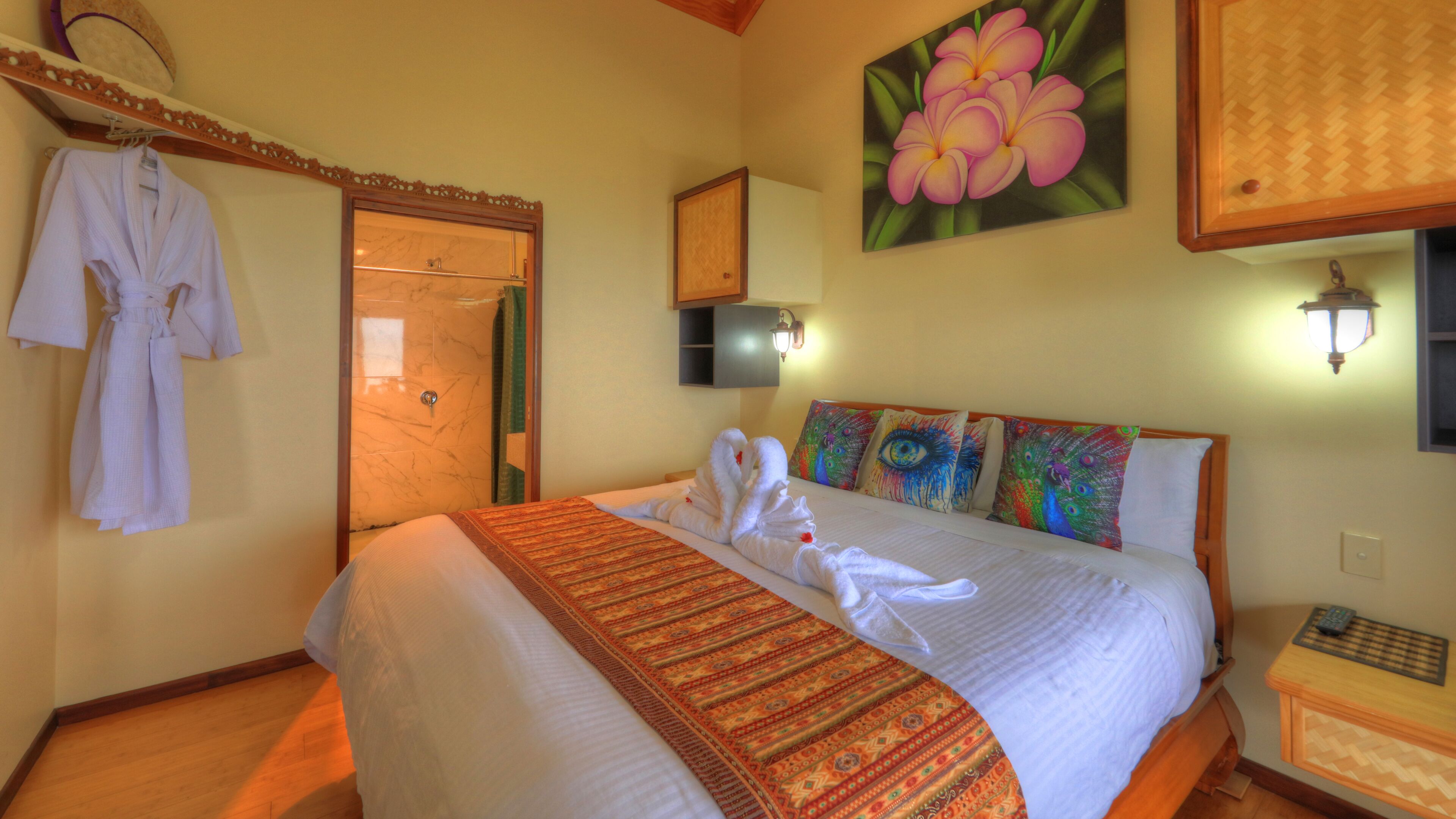 A hotel room with a bed, a robe hanging on the wall, a shower, and a painting of flowers.