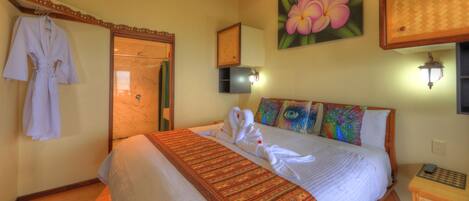A hotel room with a bed, a robe hanging on the wall, a shower, and a painting of flowers.
