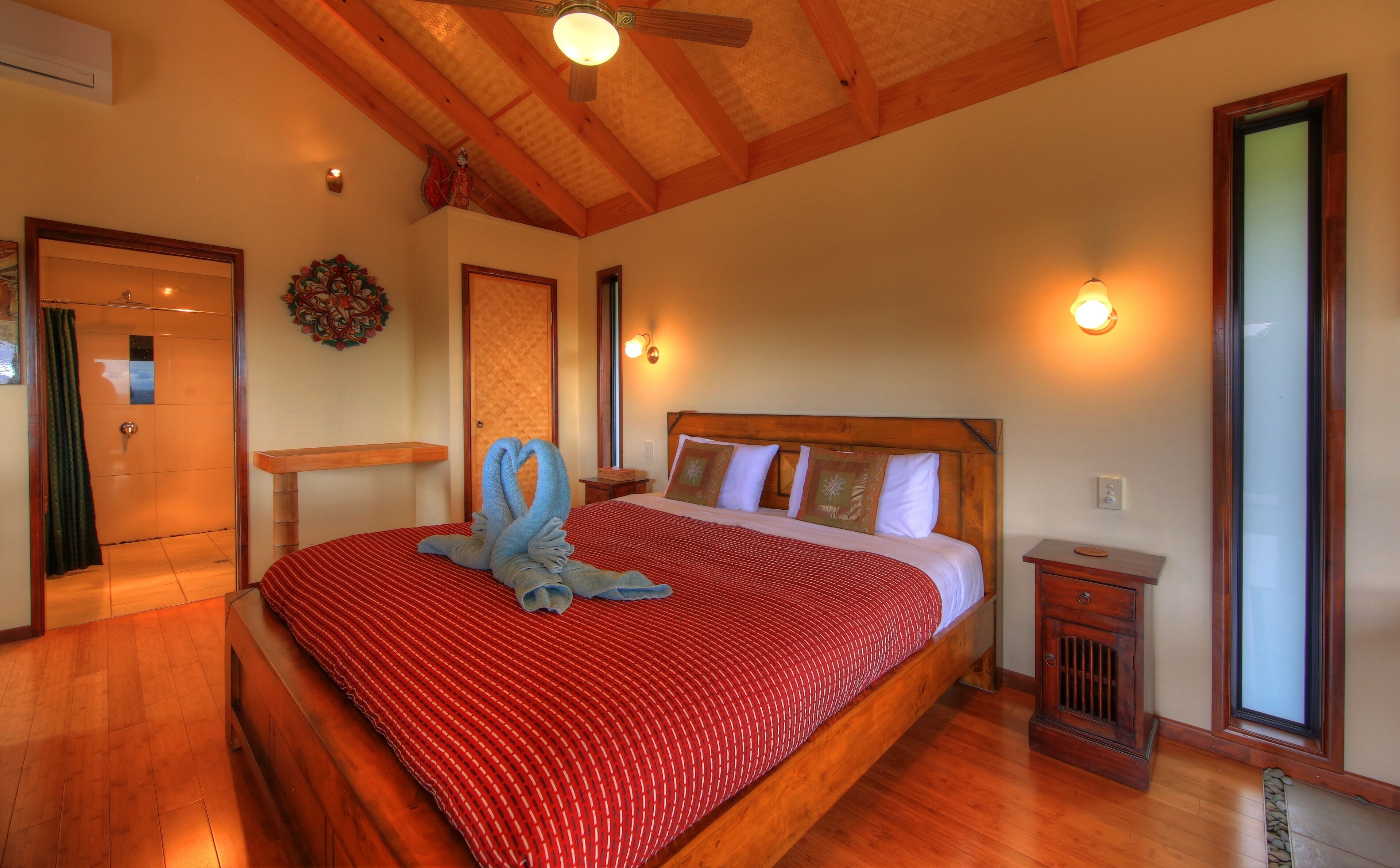 Een hotelkamer met een houten plafond, een bed met een rood-witte strepen dekbedovertrek, een houten nachtkastje en een klein houten tafeltje.
