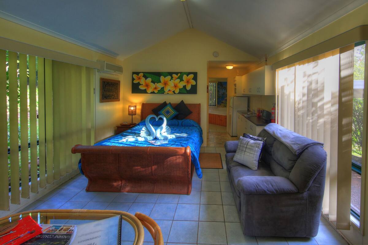 A bedroom with a bed, a sofa, a dining table, and a kitchen area.
