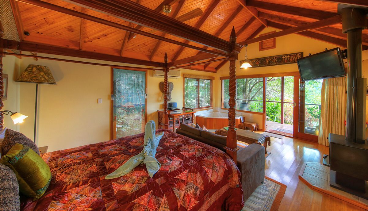 A cozy room with a large bed, a wooden ceiling, a fireplace, and large windows offering a view of the outdoors.