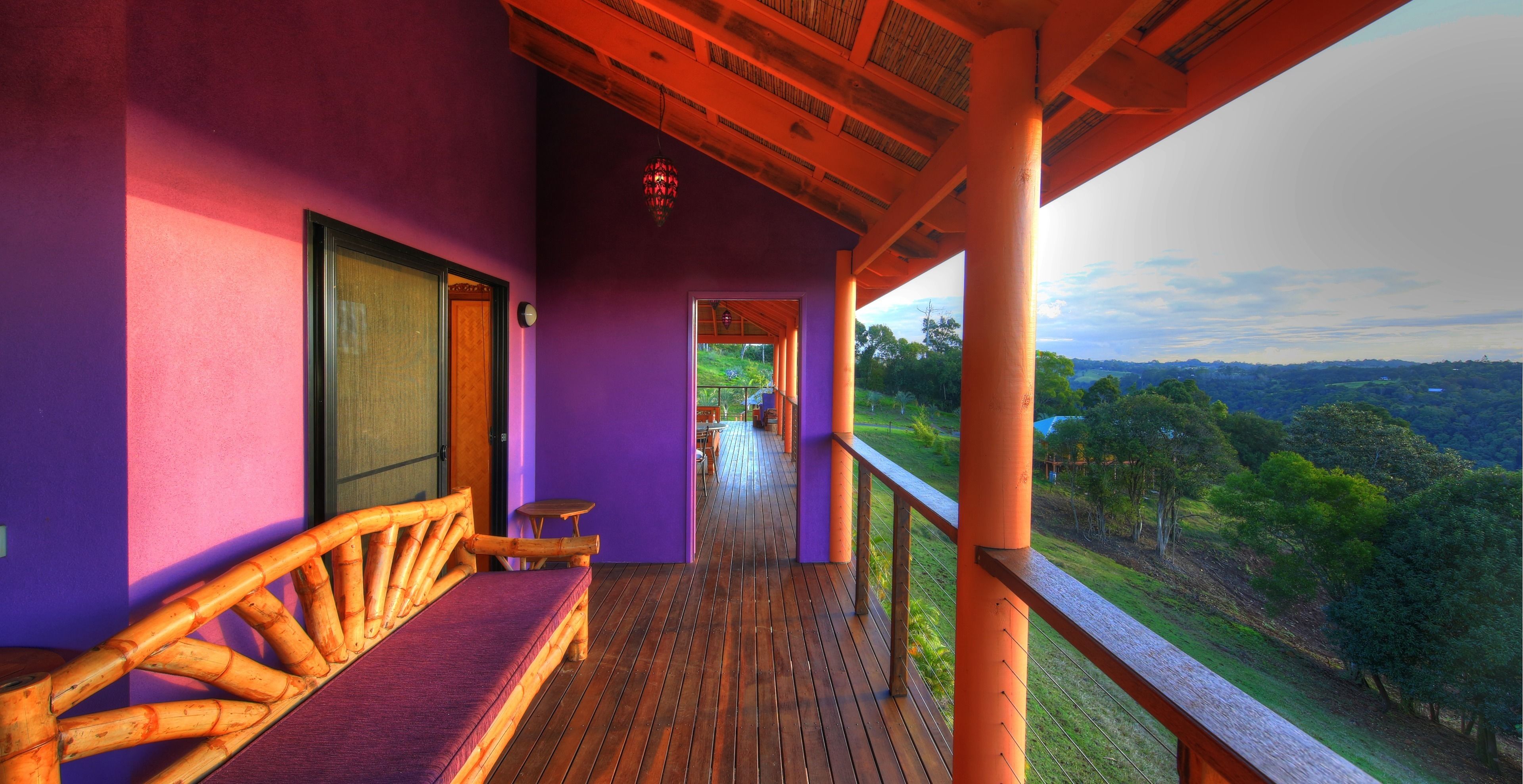 Une terrasse en bois avec un mur violet et une vue sur un paysage verdoyant.