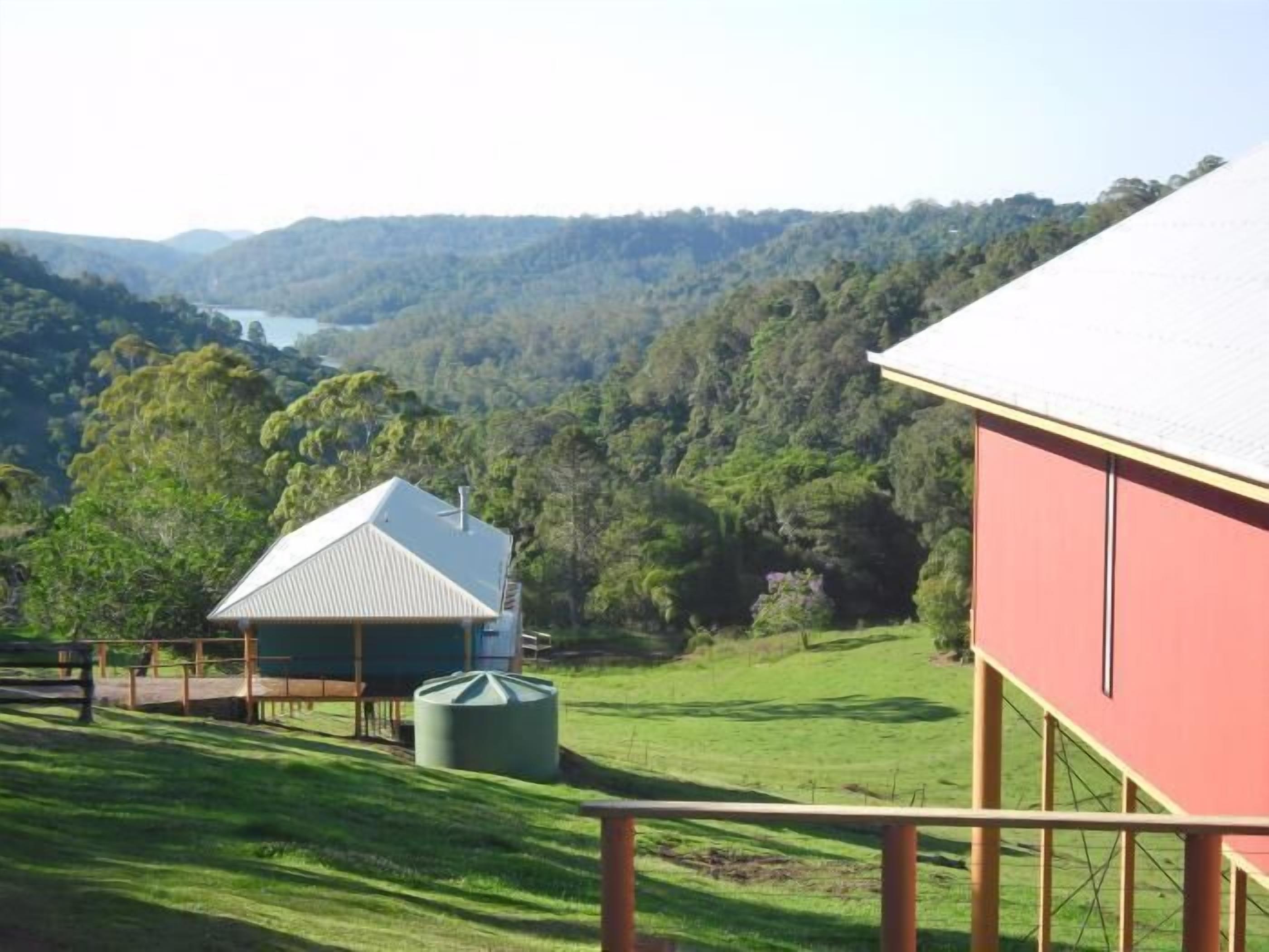 Um edifício vermelho com telhado branco, uma estrutura cilíndrica verde e vista para um vale exuberante com um lago ao longe.