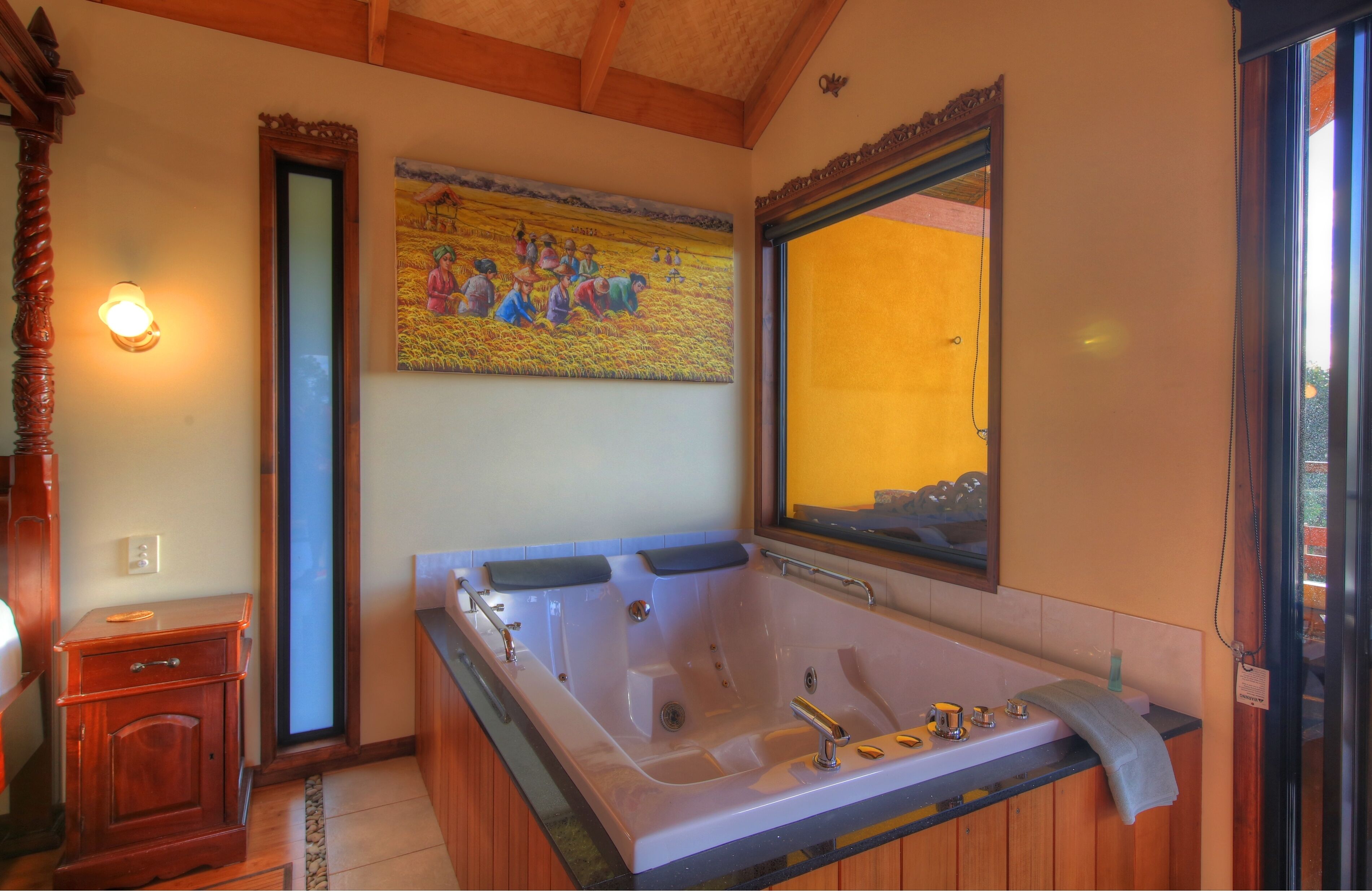 Un baño con una bañera grande, muebles de madera, un cuadro colgado en la pared y una ventana con vistas.