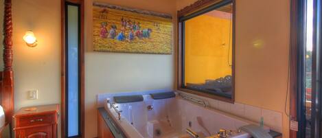 Un baño con una bañera grande, muebles de madera, un cuadro colgado en la pared y una ventana con vistas.