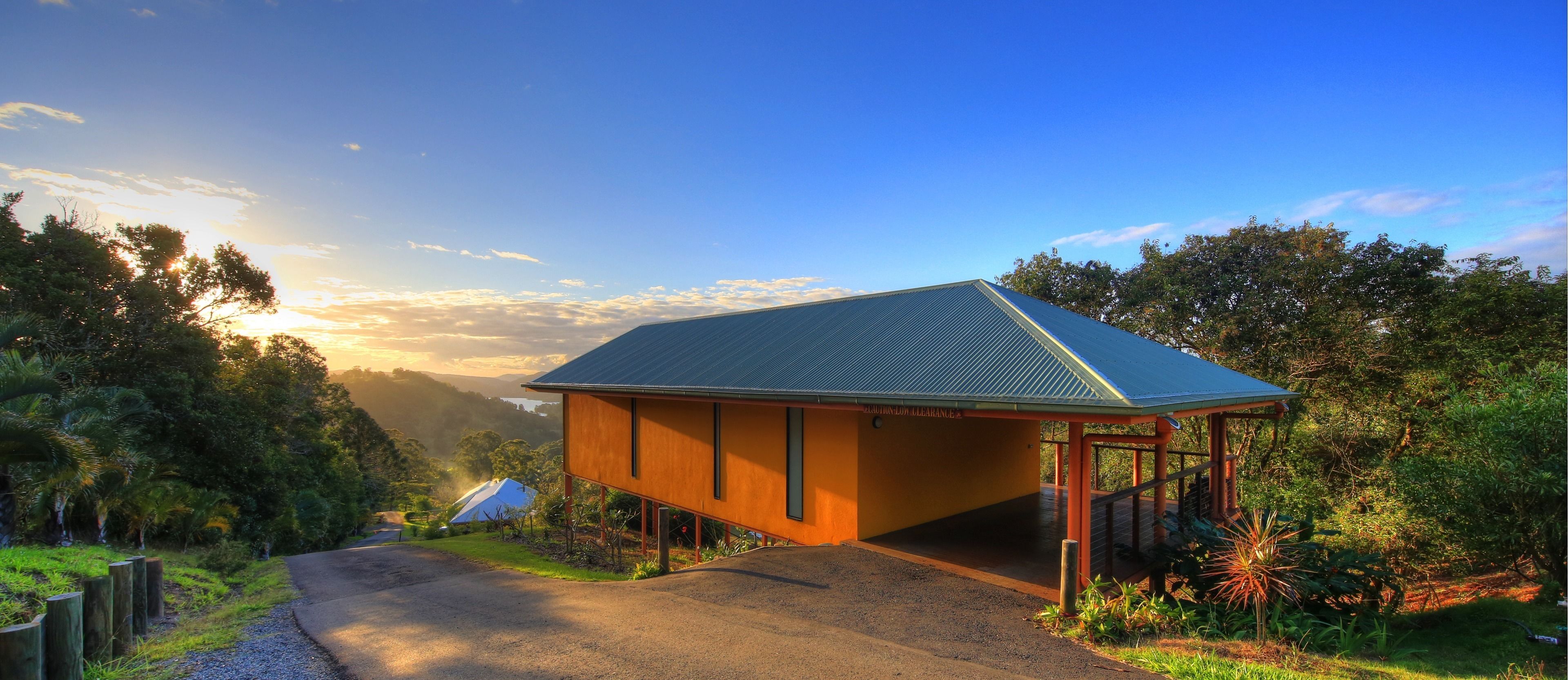 A modern building with a sloped roof, surrounded by lush greenery and a clear sky.