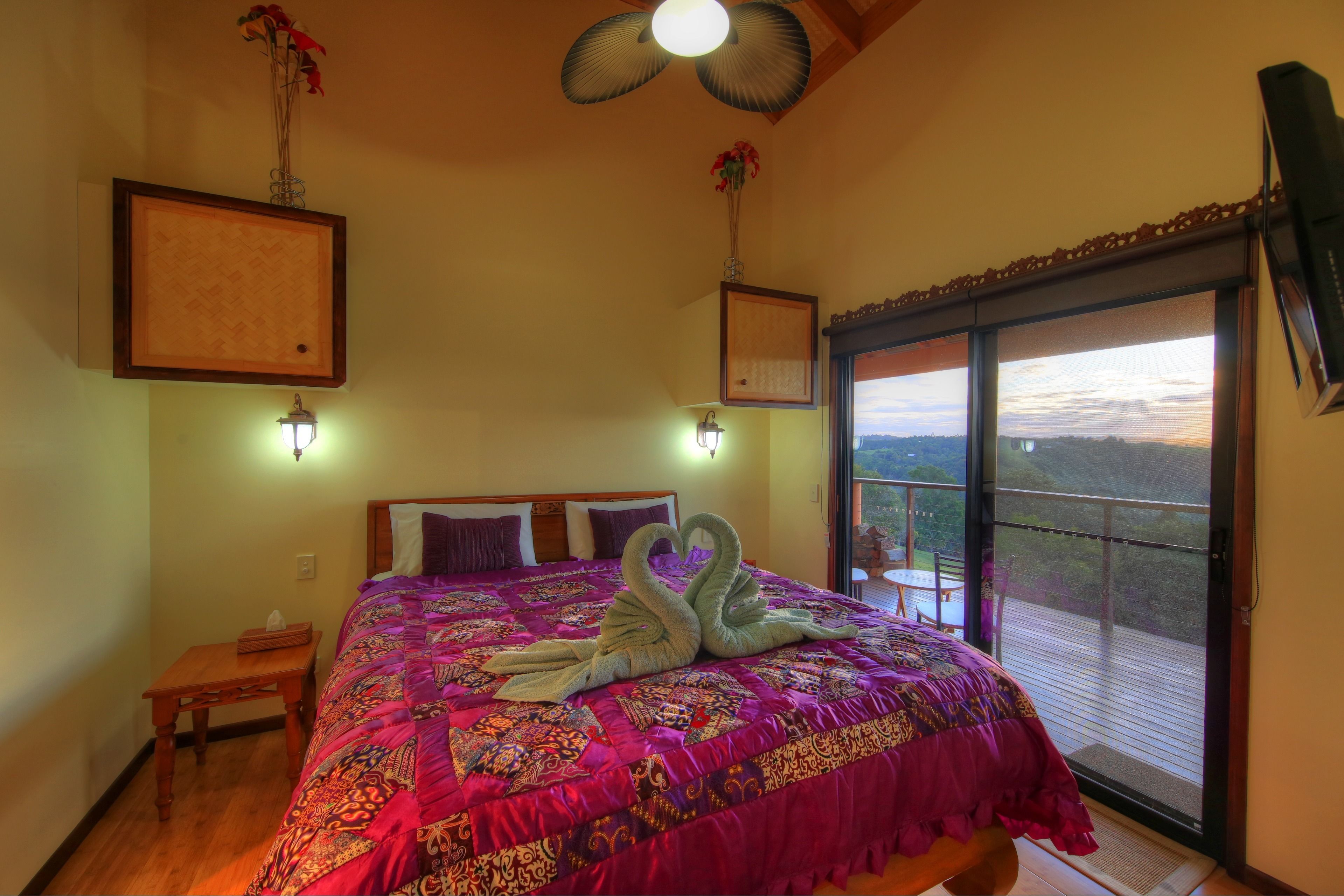 A bedroom with a large bed, two wall-mounted lights, a wooden nightstand, and a view of the outdoors through a sliding glass door.