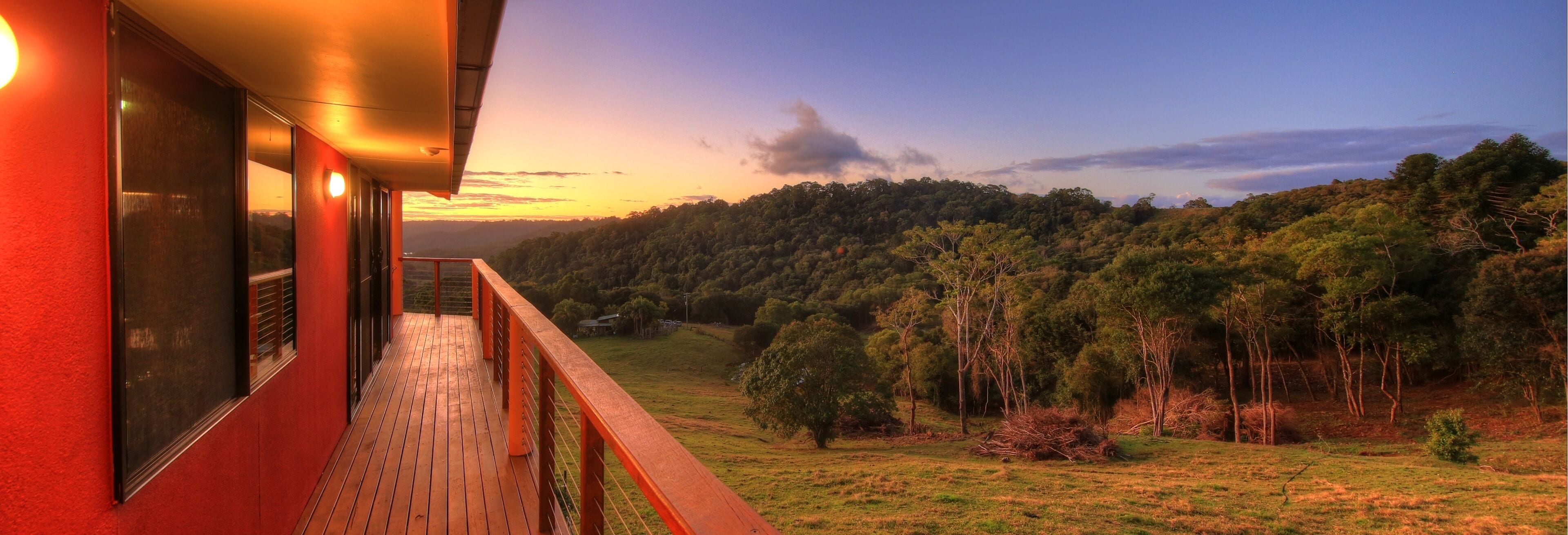 A balcony with a view of a forested hillside during sunset.