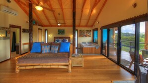 Quarto espaçoso com uma cama grande, piso de madeira, ventilador de teto e vista para o exterior por uma porta de vidro deslizante.