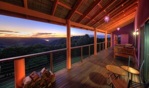 Une terrasse en bois offrant une vue sur une vallée, une table et des chaises, ainsi qu’une pile de bois de chauffage.