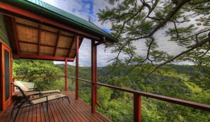 Une terrasse en bois dotée d’un espace salon couvert, offrant une vue sur un paysage verdoyant et luxuriant.
