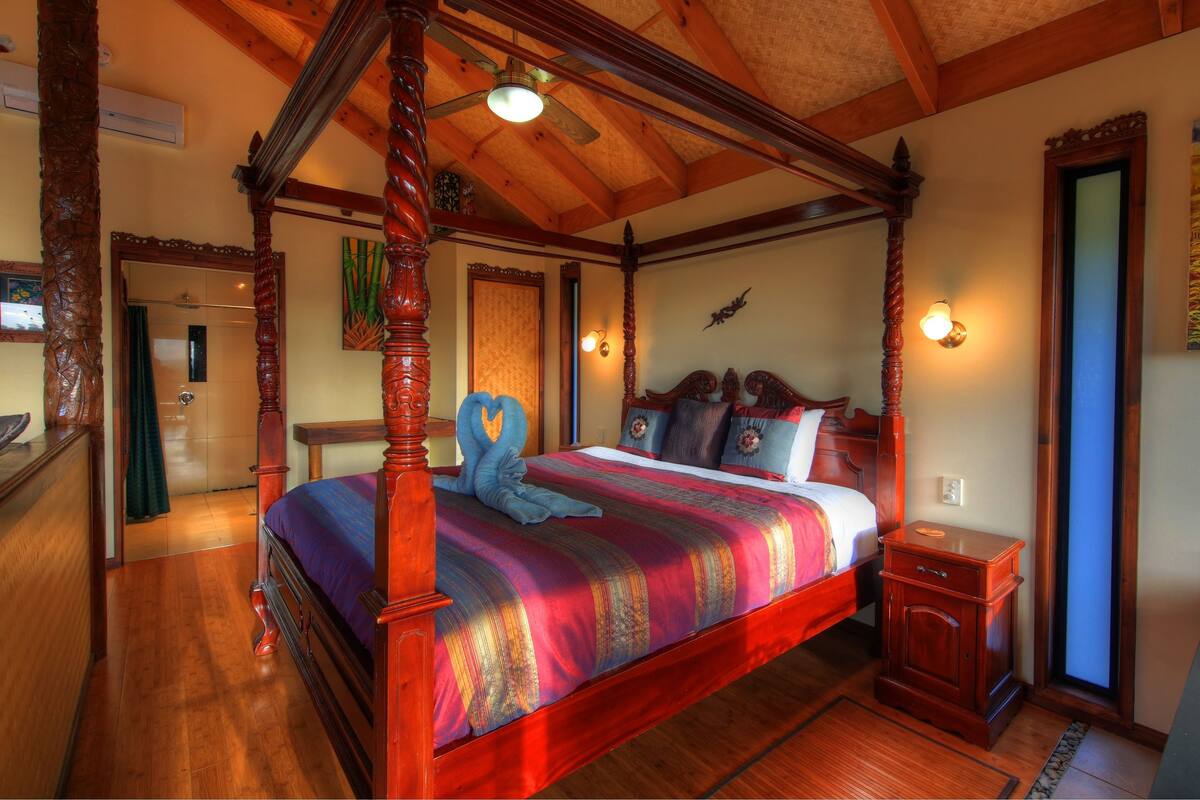 A four-poster bed with a colorful bedspread, a wooden nightstand, and a painting on the wall.