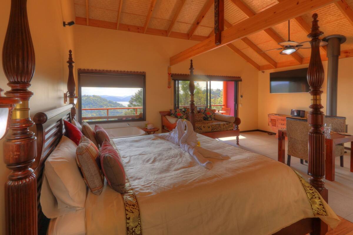 A spacious bedroom with a large bed, a view of the outdoors, and a dining area.