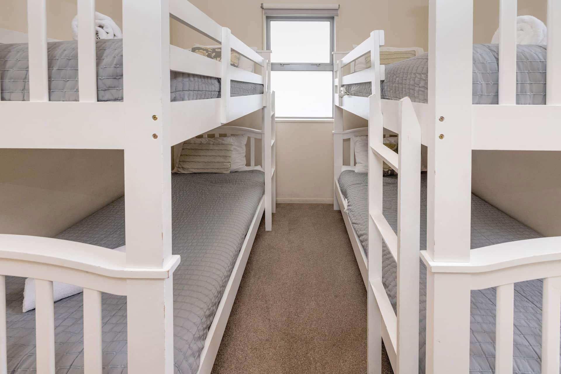 Een slaapkamer met stapelbed, raam, vloerbedekking en witte leuningen.