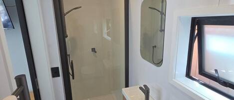 Een moderne badkamer met een douchecabine van glas, een wastafelmeubel met een wastafel en een spiegel.