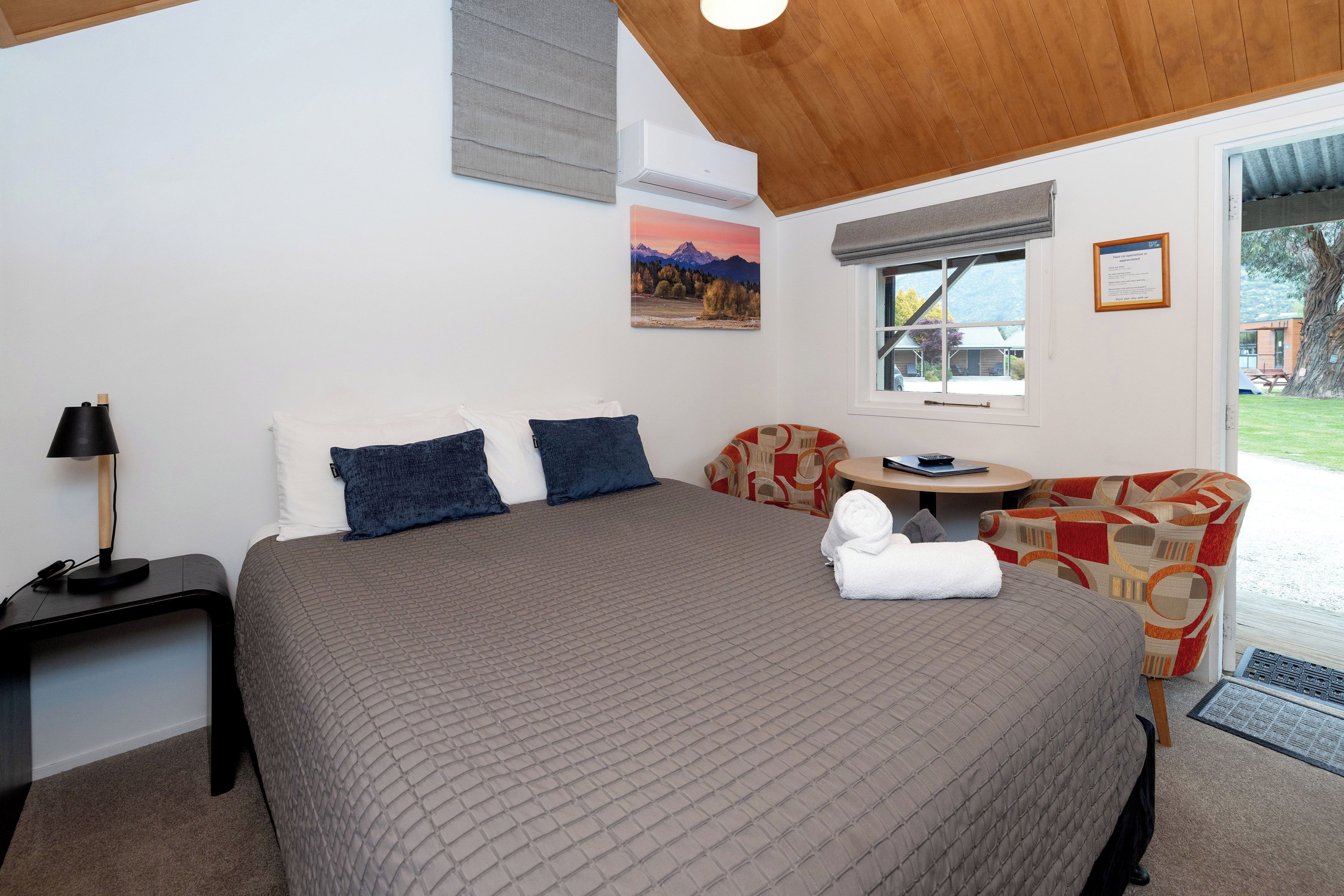 A hotel room with a large bed, a small table, a chair, and a window with a view of the outside.