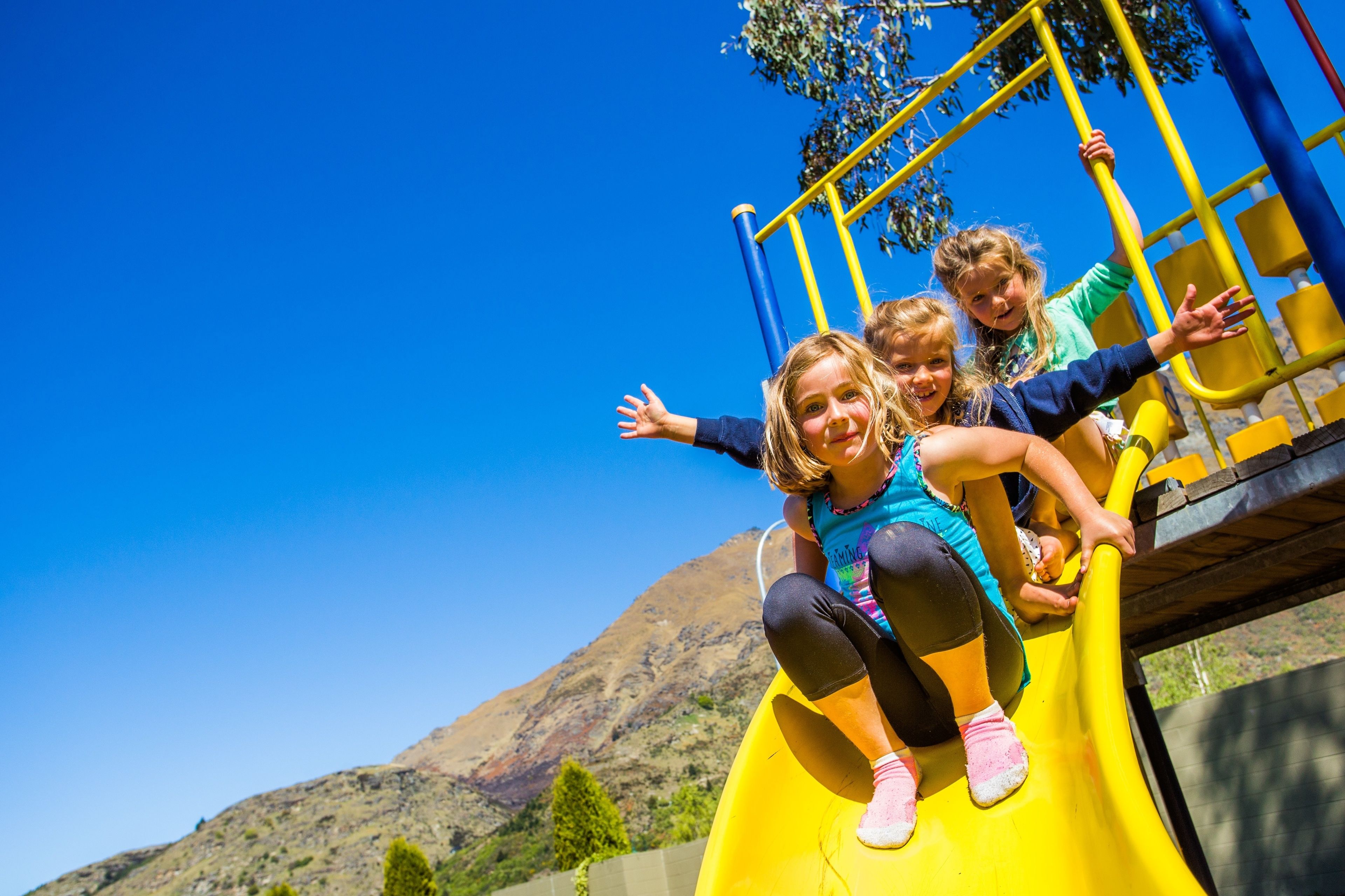 A playground with a yellow slide, surrounded by a clear blue sky and a mountain in the background.