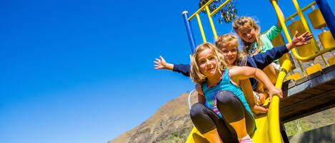 A playground with a yellow slide, surrounded by a clear blue sky and a mountain in the background.