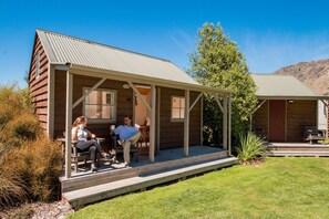 A rustic log cabin with a porch, a small deck, and a mountain backdrop. - Queenstown TOP 10 Holiday Park (Arthur's Point)