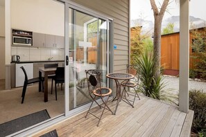 A modern kitchen with a microwave and cabinets, a dining area with a table and chairs, and a wooden deck with a view of a tree and mountains. - Queenstown TOP 10 Holiday Park (Arthur's Point)