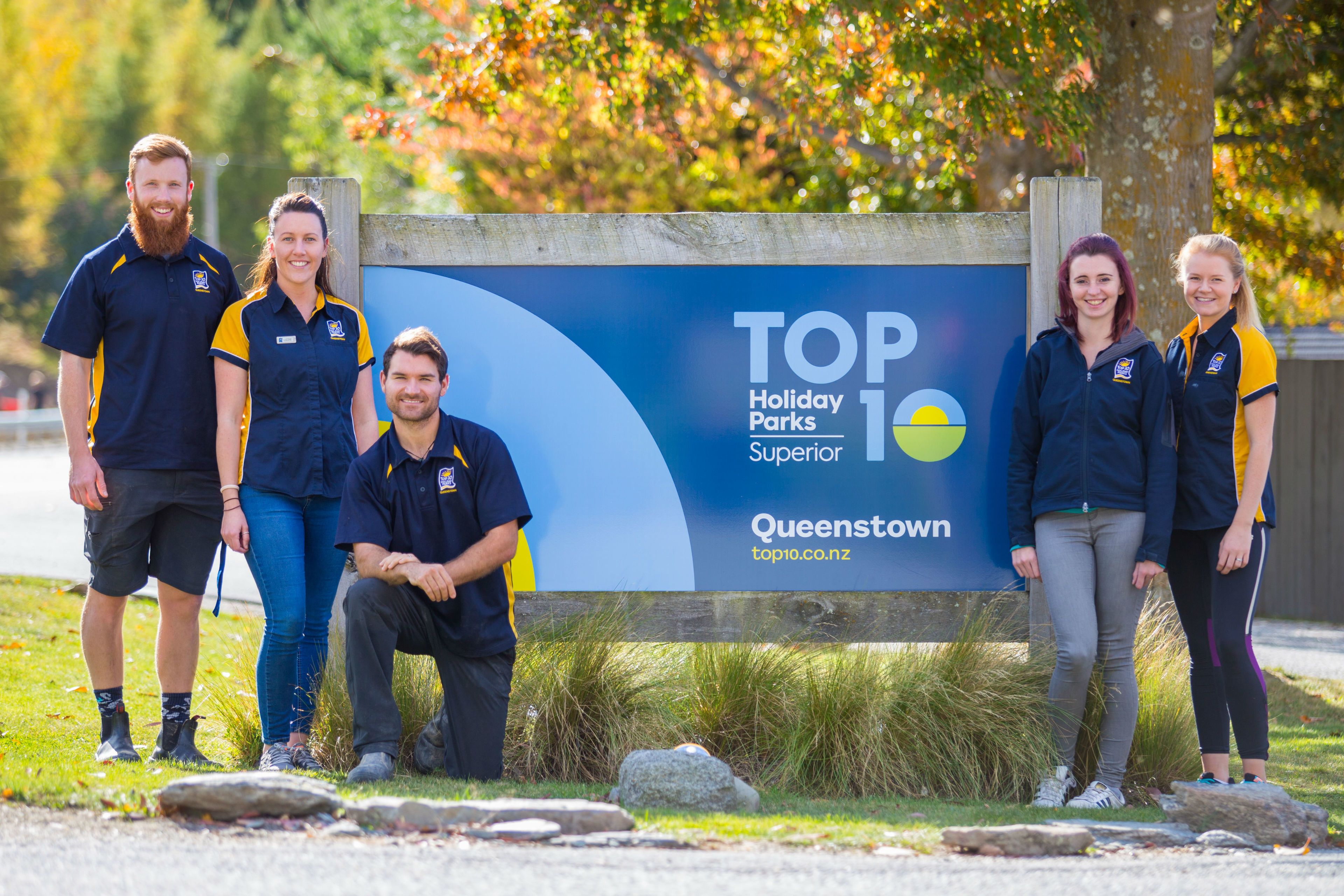 A group of people standing in front of a sign that reads "TOP Holiday Parks Superior Queenstown".