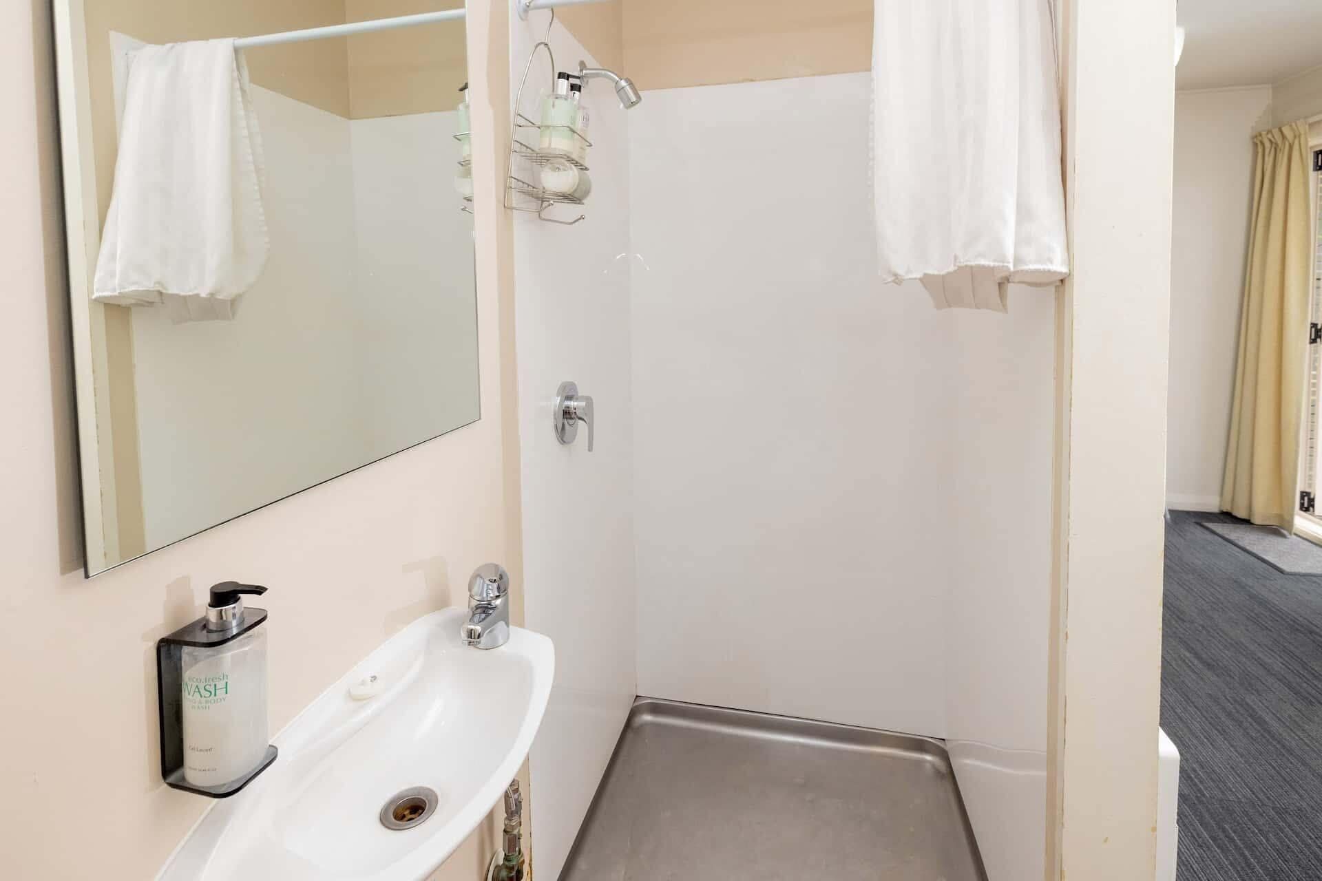 A bathroom with a white sink, a mirror, a shower, and a towel rack.