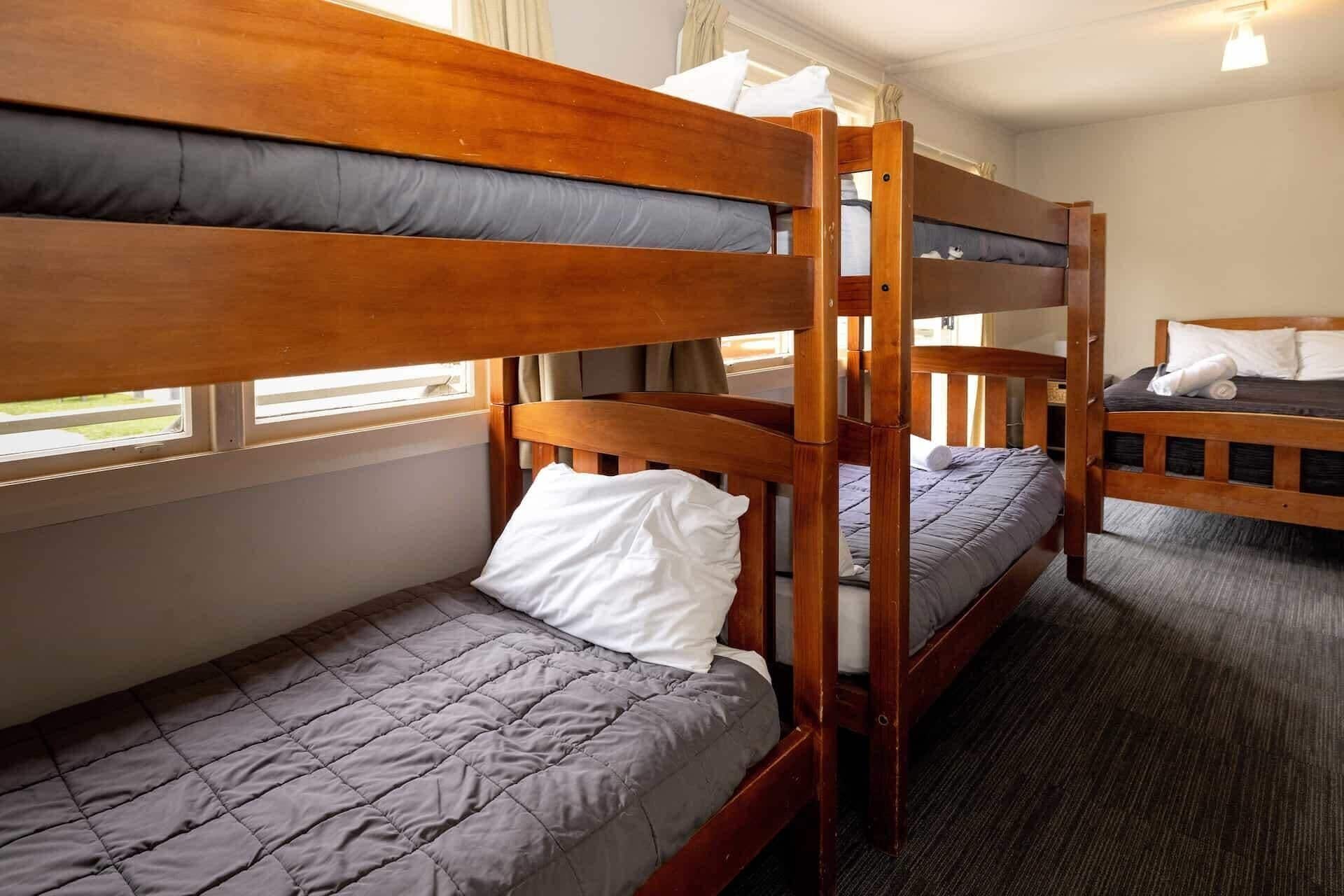 A dormitory room with bunk beds, a window, and a carpeted floor.