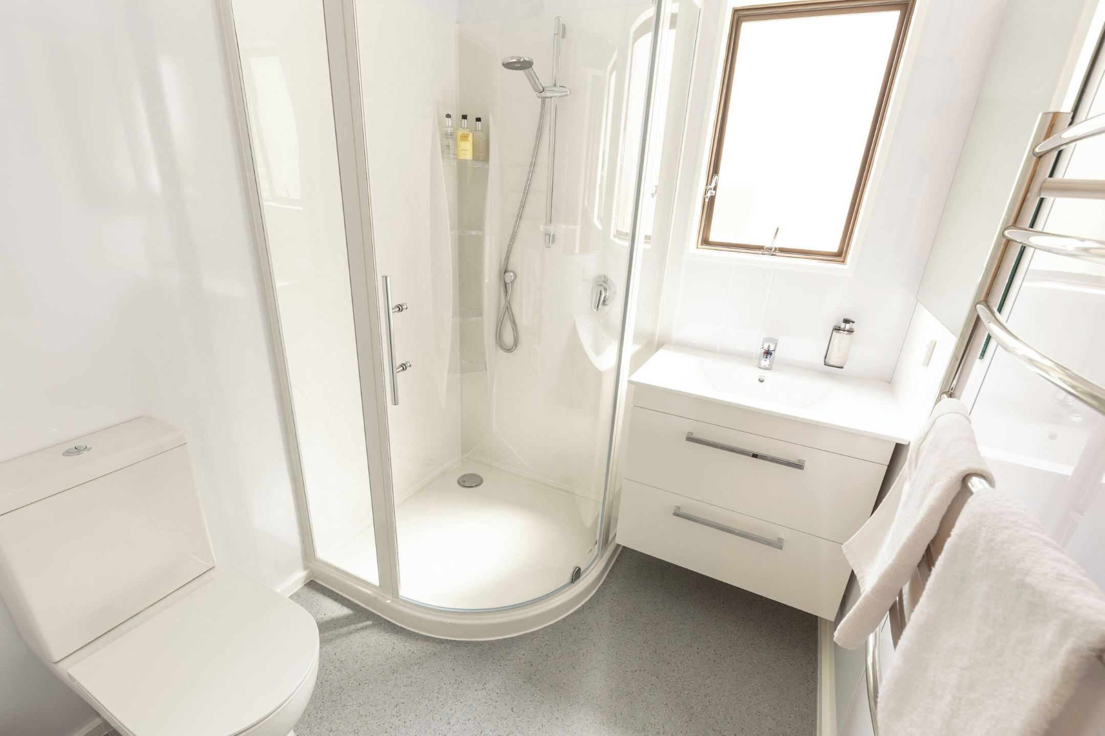 Une salle de bain moderne avec une douche à parois de verre, des toilettes blanches, un lavabo avec un miroir et un porte-serviettes.
