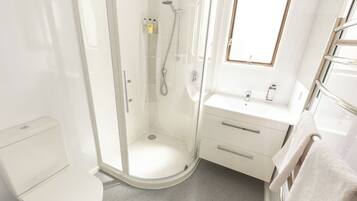 Une salle de bain moderne avec une douche à parois de verre, des toilettes blanches, un lavabo avec un miroir et un porte-serviettes.