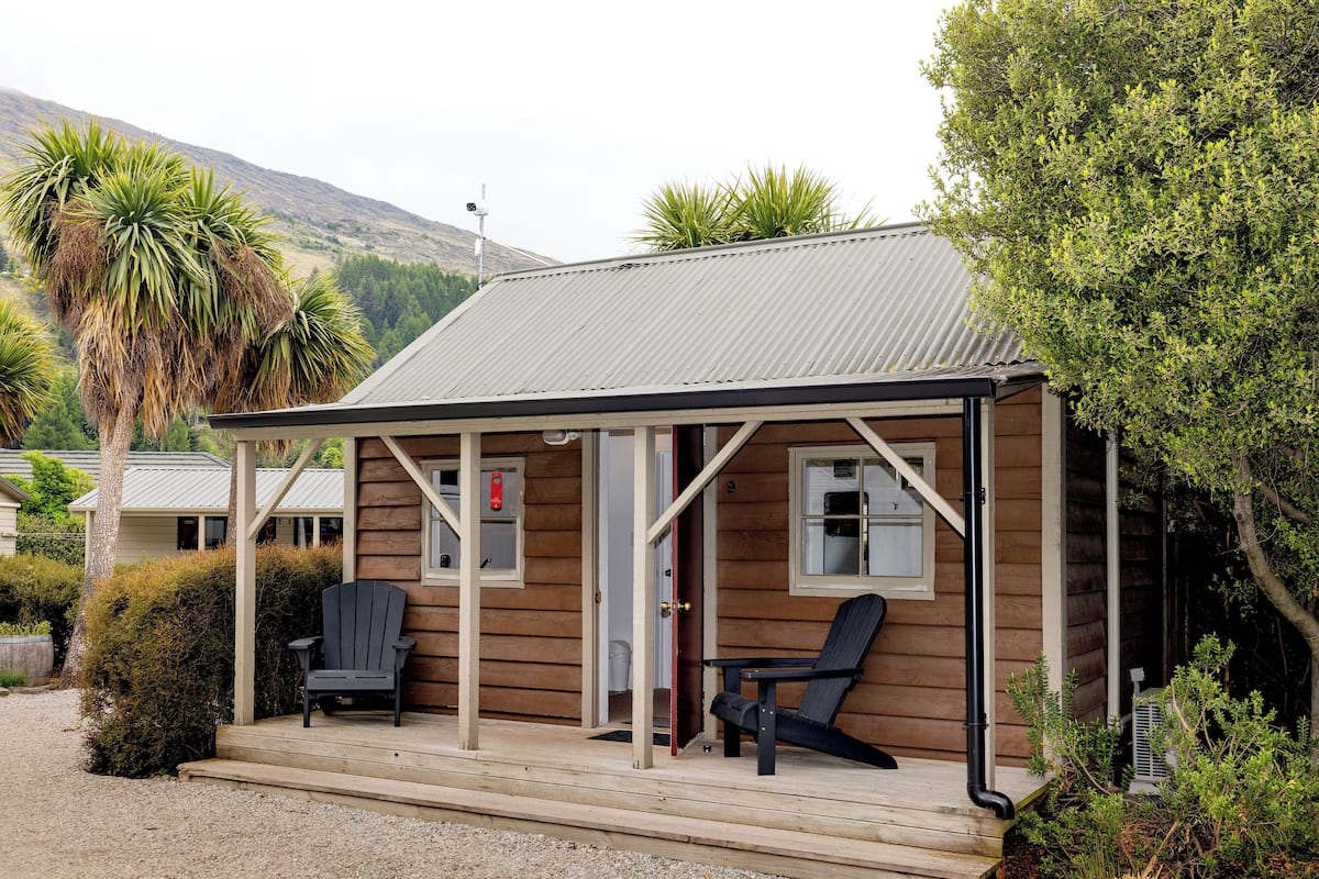 A wooden cabin with a porch, two chairs, and a small table.