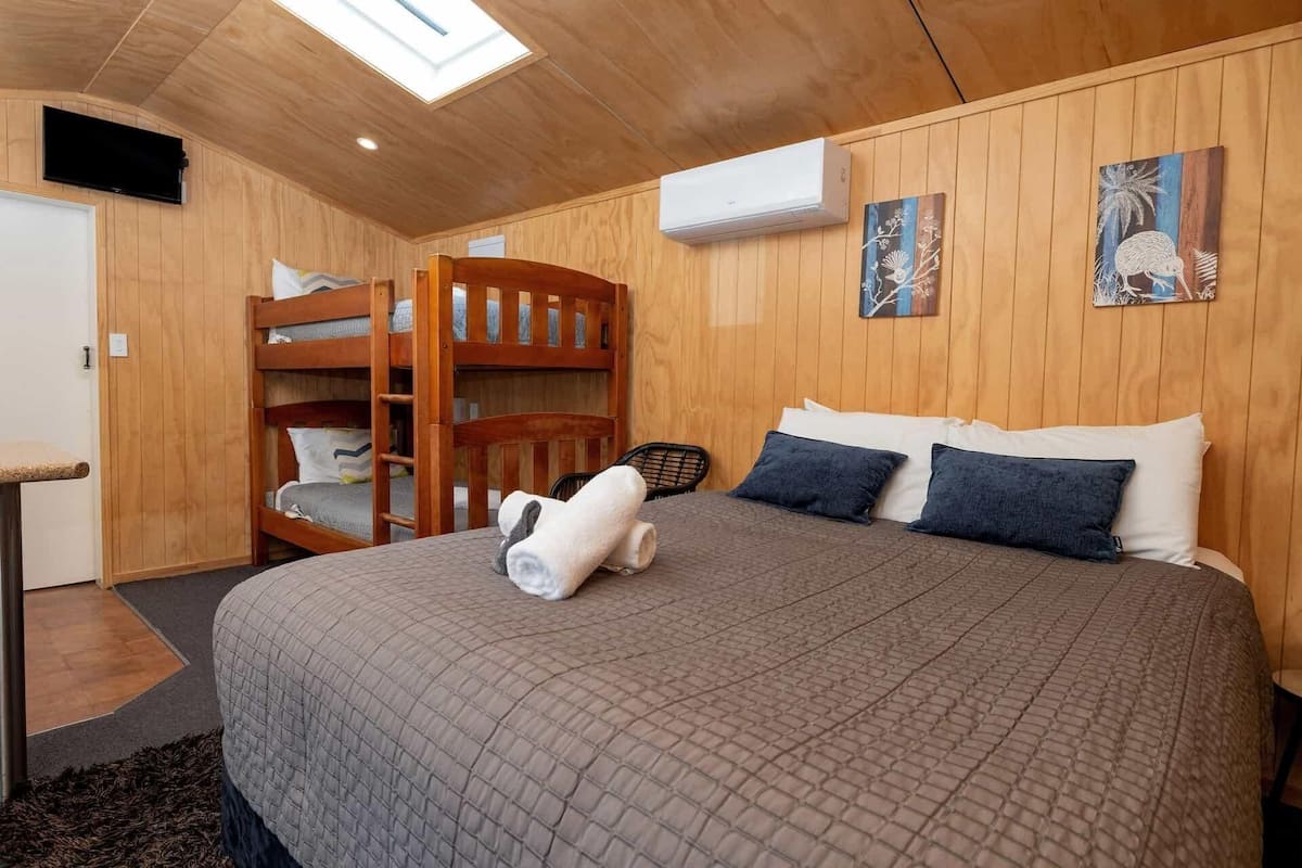 A wooden room with bunk beds, a flat-screen TV, an air conditioner, and artwork on the walls.