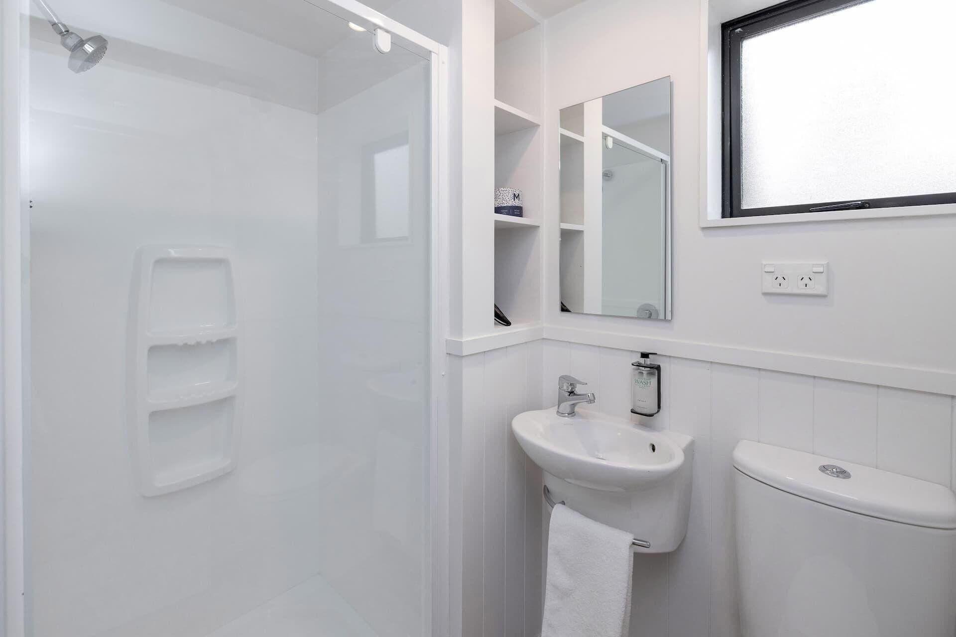 Un baño moderno con cabina de ducha, lavamanos, inodoro y espejo sobre el lavamanos.
